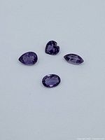 Close-up photo of four loose amethyst gemstones of different cuts on a white background, showing their color and shapes.