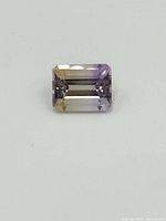 Top view of rectangular emerald cut ametrine with purple and yellow hues on white background.