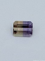 Top view photograph of rectangular faceted ametrine gemstone showing color zoning of purple and yellow.