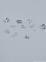 Several loose transparent light blue to pale violet gemstones with mixed shapes and cuts, laid flat on light grey surface.