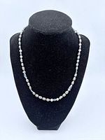 Black pearl necklace displayed on black velvet bust showing the dark colored pearls and silver accent beads