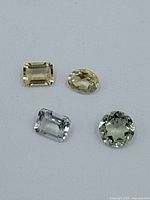 Four faceted gemstones in light yellow, pale blue, and green colors on grey surface.