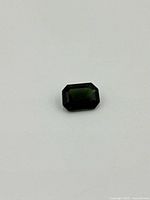 Octagonal dark green demantoid garnet gemstone on white background displaying the stone's color and cut.