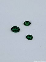 Three oval faceted green Demantoid garnet gemstones arranged on white background.