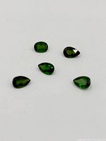 Five loose demantoid garnet gemstones on white background in mixed shapes.