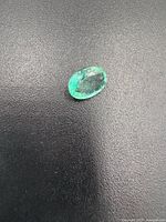 Close-up of the oval green emerald gemstone with visible inclusions on a black surface.