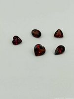 Five garnet gemstones of various cuts on white background.