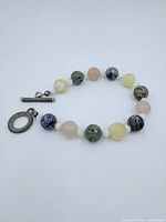 Bracelet of assorted round gemstone beads in pink, yellow, blue-gray, and gray-green with metal toggle clasp on white background.