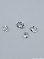 Four faceted gemstones placed on a surface shown in natural light to detail their shape and clarity.