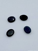 Three loose faceted oval black to blue gemstones on white background.