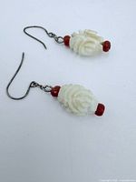 Close-up of the pair of carved white rose shaped bead earrings with red beads and black metal hooks taken on white background.