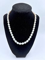 Full view of pearl necklace displayed on black bust, showing length and shape.