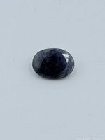 Oval sapphire gemstone showing dark blue color, faceted surface and some internal inclusions.