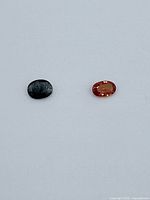 Photo of two oval-shaped sapphire gemstones, one dark blue and the other vibrant orange, placed on a neutral background for clear visibility.