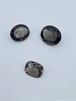 Three faceted smoky quartz gemstones arranged on a light gray surface, showing color and cuts from above and angles.