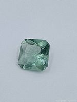 Top view of a green spinel gemstone showing square cushion cut with visible facets and transparency.
