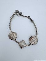 Bracelet close-up showing clasp, chain extension with heart charm, and textured triangular and square silver links.