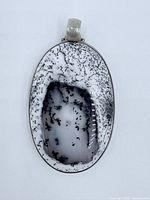 Front view of oval dendritic opal pendant with visible black dendritic patterns in white and translucent stone set in sterling silver.