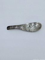 Front of spoon-shaped sterling silver pendant showing Indigenous engravings.