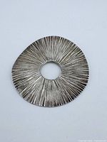 Front view of sterling silver pendant showing textured radiating line design.