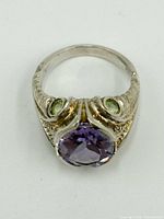 Close-up angled view of the sterling silver ring with a large oval purple stone and two smaller green stones on the sides, showing band details.