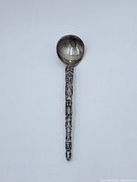Silver totem spoon laid out vertically showing the round bowl and detailed carved totem pole design on the handle.