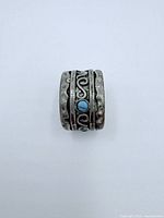 Front view of the wide sterling silver ring with turquoise stones and oxidized swirl detailing.