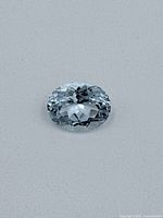 Topaz gemstone placed on white background showing oval cut, brilliant facets, and light blue color.