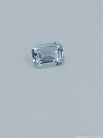 Light blue rectangular emerald cut topaz gemstone on a plain white surface showing its shape and faceting