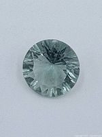 Close-up of round cut pale blue topaz gemstone showing facets and internal inclusions.
