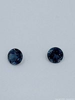 Front view of two round blue topaz gemstones showing their deep blue color and faceted cuts.