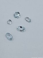 Five various-shaped faceted light blue topaz gemstones on white background showing clarity and cuts.