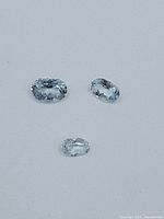 Three loose oval topaz gemstones shown on a gray background.