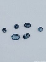 Five faceted blue topaz gemstones displayed on a white background.