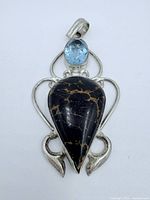 Front view of the topaz and black stone sterling silver pendant showing the pear-shaped black stone with gold veining and oval blue topaz on top in silver setting.