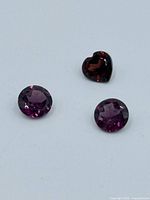Three loose faceted tourmaline gemstones on a white background, showing two round stones and one heart-shaped stone.