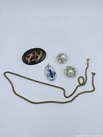 Overview of the jewelry lot showing all items together: brooch, porcelain pendant, pearl earrings, and gold-tone necklace