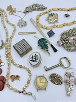 Various jewelry pieces including necklaces, brooches, rings, watch, key pendant and decorative boxes arranged for photos.