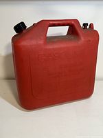 Front angle view of red plastic gasoline can showing main handle and twist cap lid.