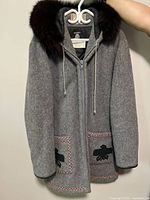 Front view of grey wool coat with fur trimmed hood, patch pockets and leather cuffs