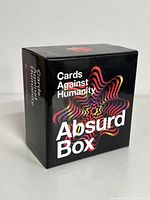 Front view of the black box with colorful starburst design showing the product name 'Cards Against Humanity Absurd Box'.