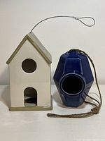 Cream ceramic birdhouse with olive roof and base, circular entry hole in front, hanging wire visible