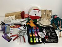 Full overview of sewing and craft supplies assortment including tools, ribbon, thread spools, doilies, knitting needles, glue sticks, punch pliers, and craft paper.