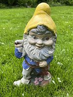 Front view of concrete garden gnome statue with chipped paint and detailed beard.