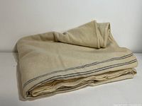 Folded beige wool blanket showing striped edges and layered folds.