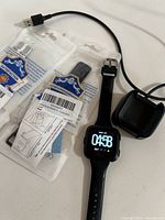 Fitbit Versa smartwatch with black wristband, two extra wristbands in packaging and USB charging cradle with cable on a flat surface.