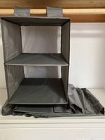 Front view of empty IKEA SKUBB hanging closet organizer showing 6 compartments with fabric shelves and mesh backing, folded flat below.