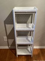 Full frontal view of the white, four-tier IKEA VESKEN plastic shelving unit standing against a beige wall on a wood floor.