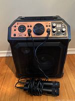 Full front view of the karaoke machine with two wired microphones placed in front, showing control panel and speaker grille.