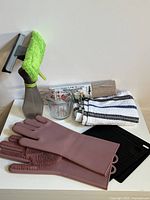 All items in lot including measuring cup, shelf liner, striped towel, pink silicone cleaning gloves with scrubbing bristles, black hot plate trivets, bottle squeegee cleaner with microfiber cloth
